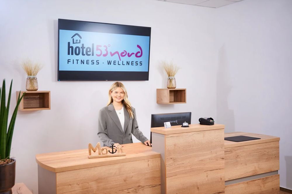 Rezeption des Hotel 53° Nord mit Holztresen und Empfangsmitarbeiterin